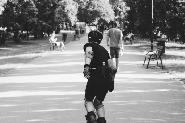 Black and white photo of a person rollerblading on a park path, captured in motion.