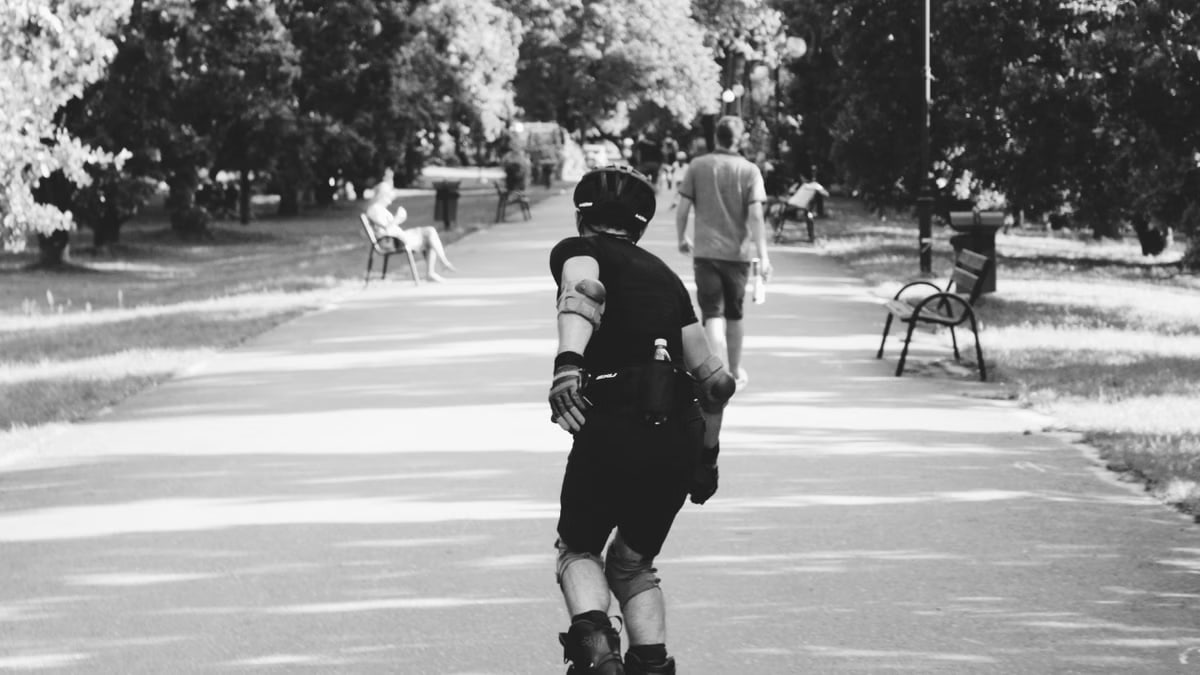 Black and white photo of a person rollerblading on a park path, captured in motion.